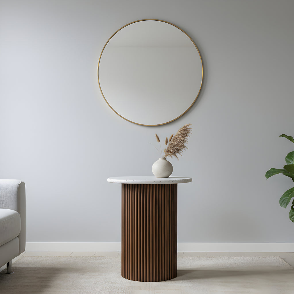 Round mirror on a light gray wall above a wooden side table with a vase and plant.