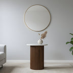 Round mirror on a light gray wall above a wooden side table with a vase and plant.