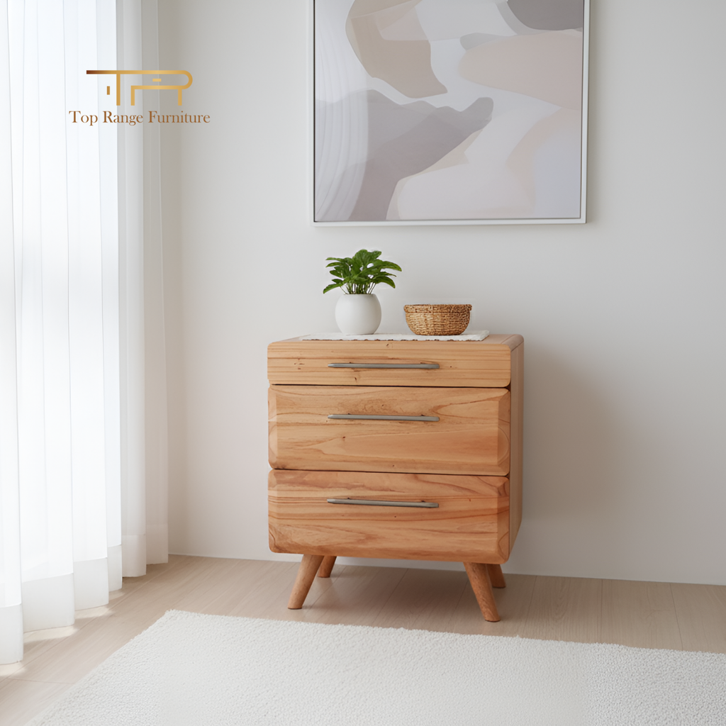 Wooden dresser with three drawers in a minimalistic room, featuring a plant and basket on top.